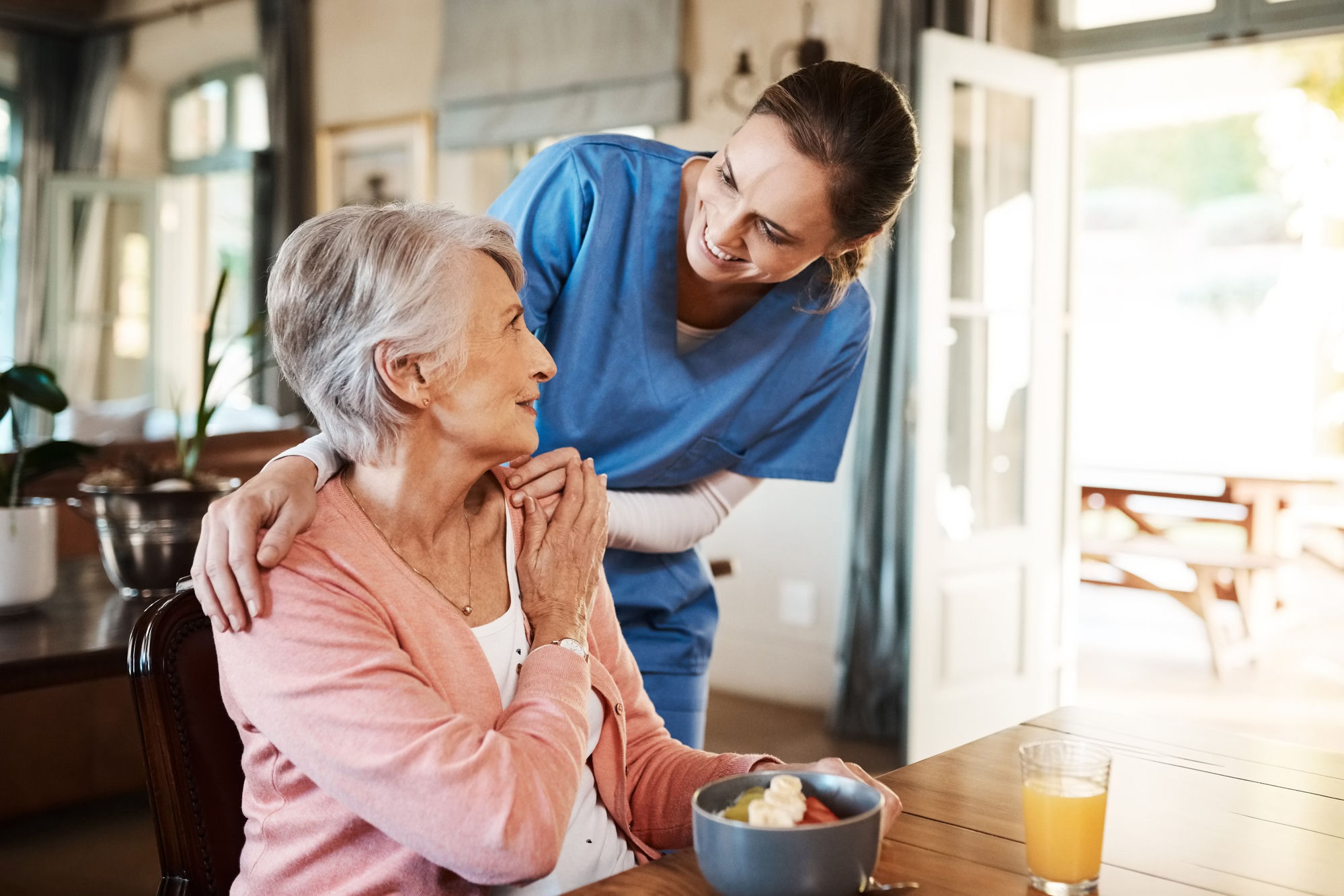 A caregiver checking in warmly with a resident over breakfast