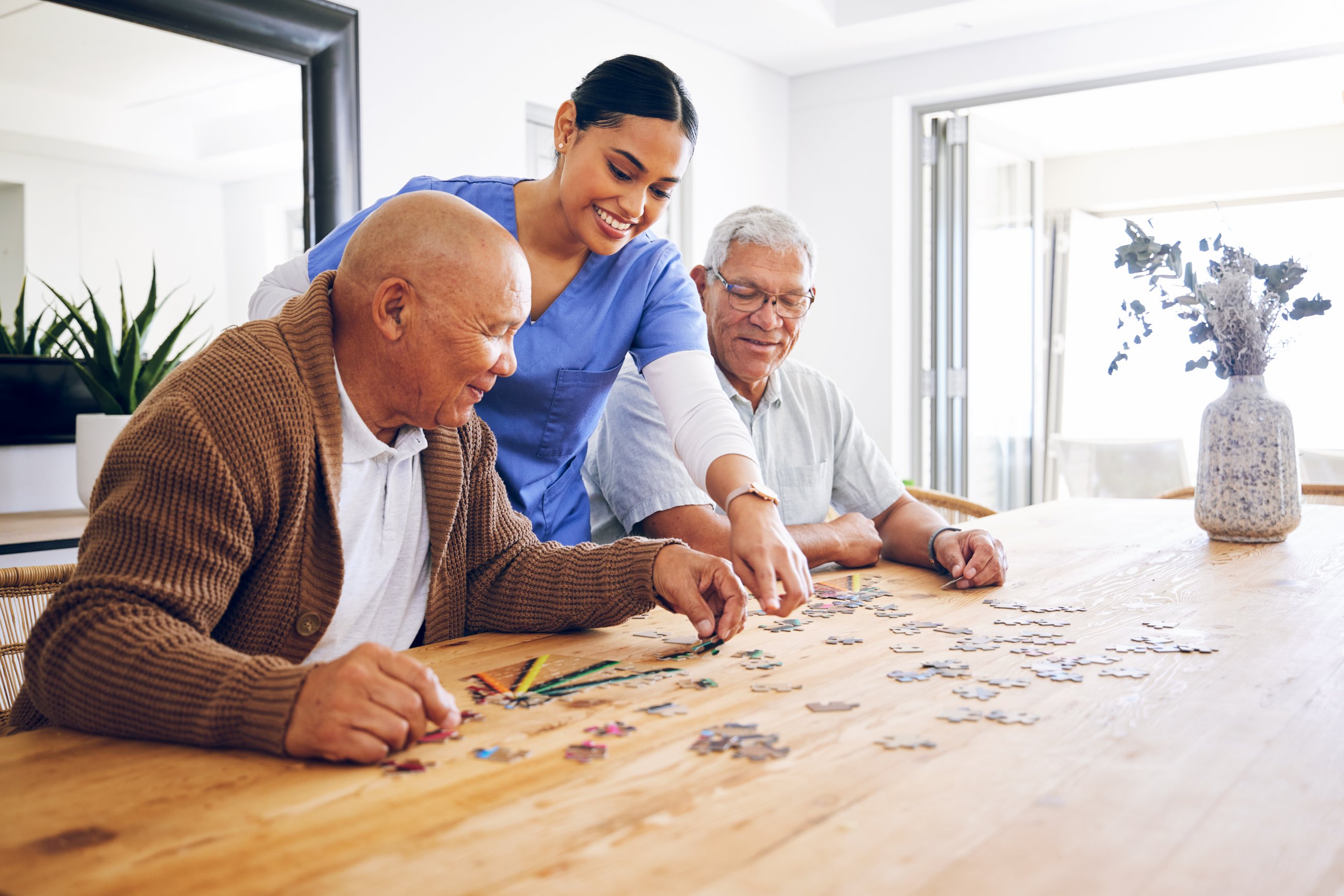 A caregiver helping two residents with a puzzle at a shared table